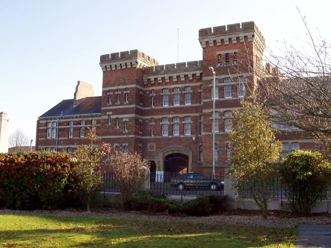 The Keep, a red-brick Victorian building with two castellated towers and an arched gateway, seen from the lawn in front.